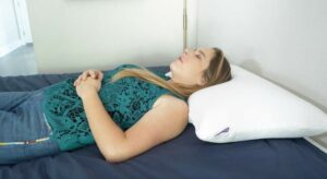 A woman rests on her back with her hands on her stomach using the Purple Harmony pillow.