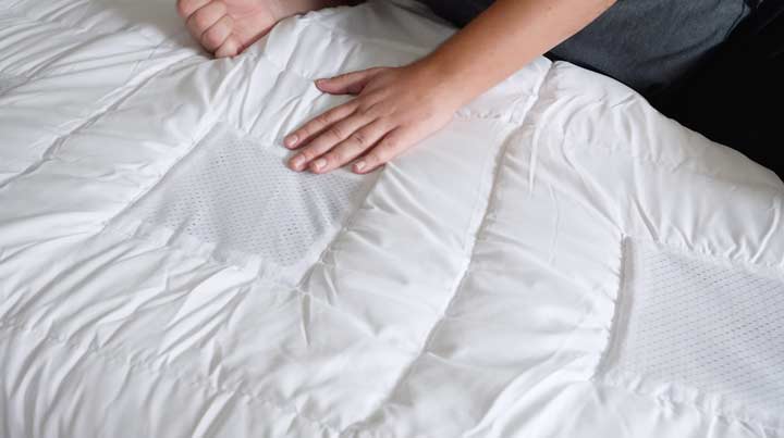 A man rubs his hand across the top of a white comforter.