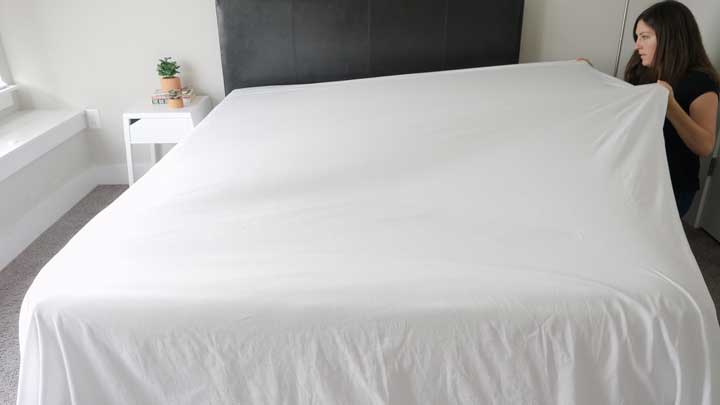 A woman lays a flat sheet across her bed