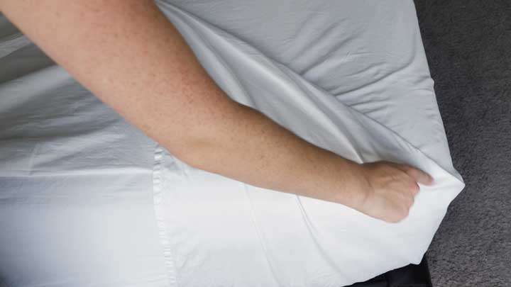 A woman folds the side of her sheet over the mattress