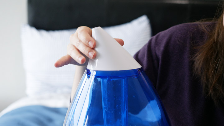 An image of a woman using the directional nozzle on the Crane Ultrasonic humidifier.