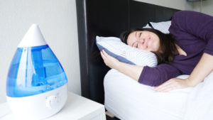 A woman sleeps on her side, facing the Crane Ultrasonic humidifier.