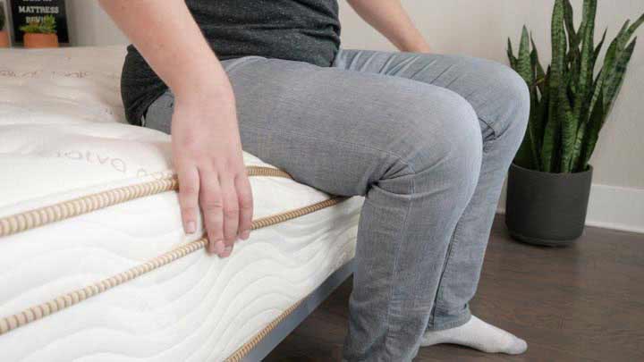 A man sits near the edge of the Saatva mattress