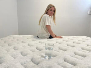 A woman looks over her shoulder at a glass of water while sitting on a Helix Dusk Luxe Mattress