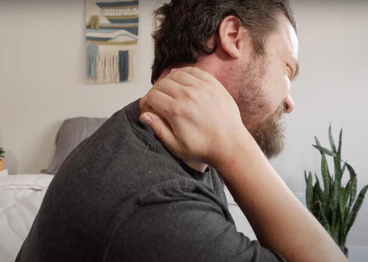 A man with a pained expression puts his hand on his neck