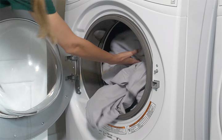 A woman puts sheets into the washing machine
