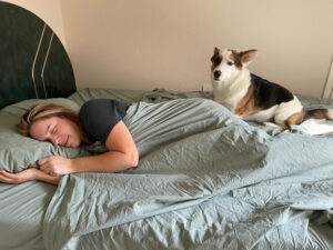 A woman sleeps on her side, with her dog, using the Tuft & Needle percale sheeets.