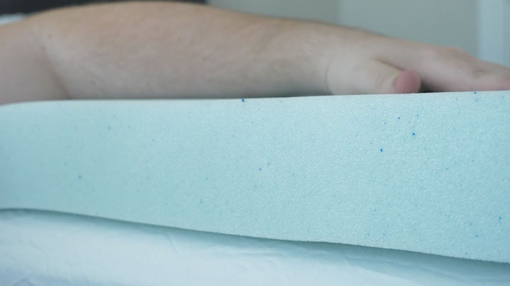 A close shot of a thick, blue mattress topper with a hand resting on top