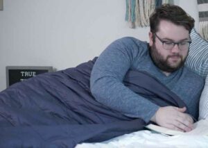 A man lounges with the Sleep Number True Temp weighted blanket while reading a book.