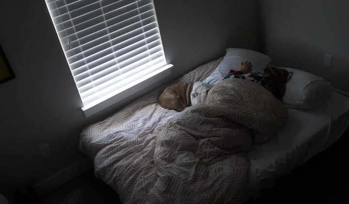 A woman sleeps with her dog on a cheap mattress