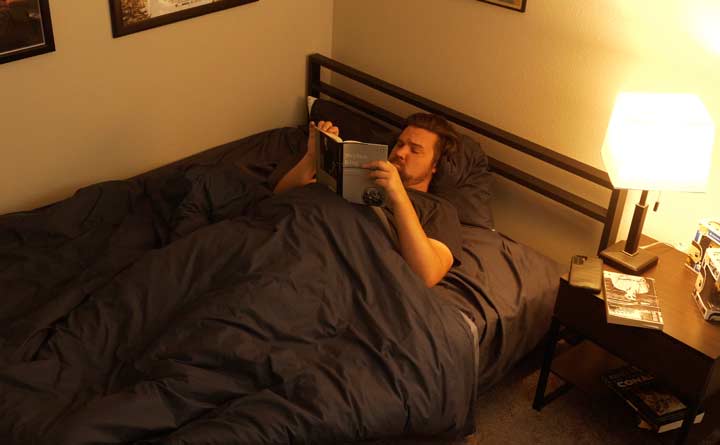 A wide shot of a man reading a book on a cheap mattress