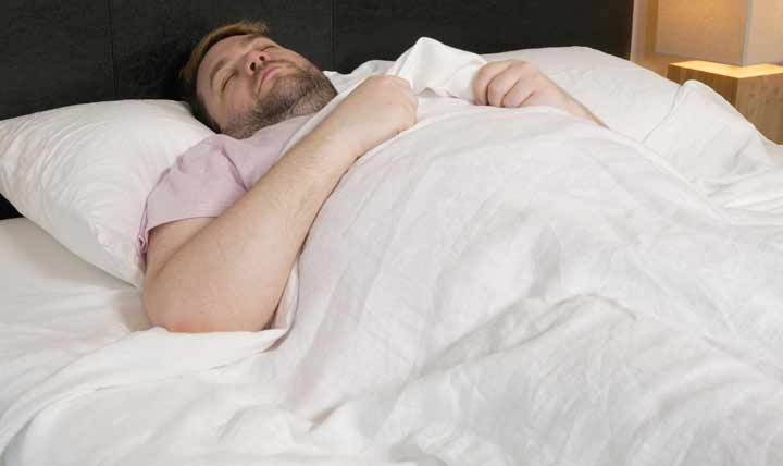A man sleeps on his back in Saatva Linen Sheets.