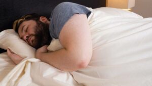 A man sleeps on his side with the Boll & Branch Percale Hemmed Sheets.