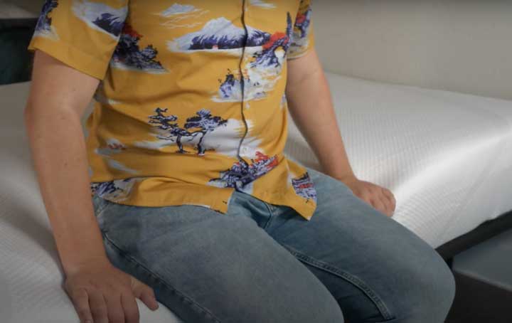 A man sits near the edge of the Tempur-Cloud Hybrid mattress