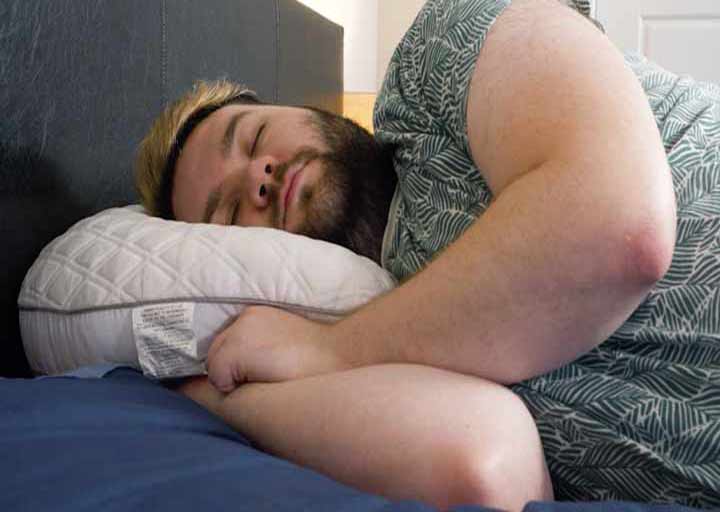 A man sleeps on his side on a Bear Contour Pillow