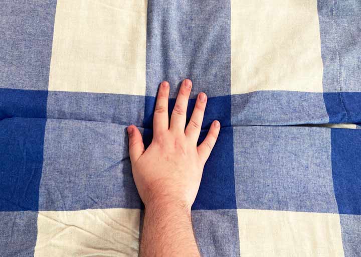 A hand rests on checkered flannel sheets
