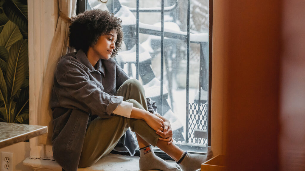 A woman looks sadly out a window in winter time