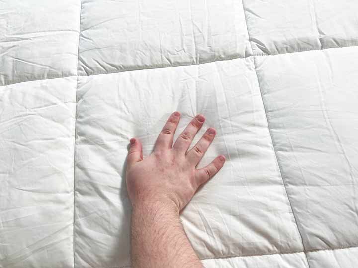 A hand glides across the Saatva comforter