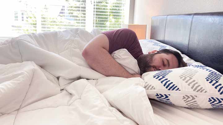 A man sleeps on his side with the Saatva comforter.