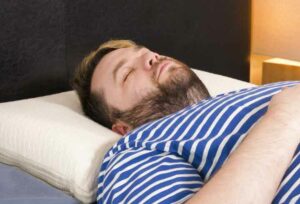 A man sleeps on his back with the Avocado Molded Latex Pillow
