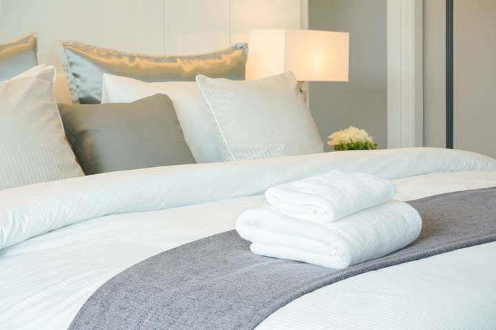 A medium shot of a hotel bed with grey throw and white towels