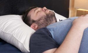A man sleeps on his back using the Plushbeds Goose Down Pillow.