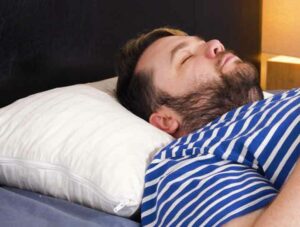 A man sleeps on his back on the Plushbeds organic shredded latex pillow.