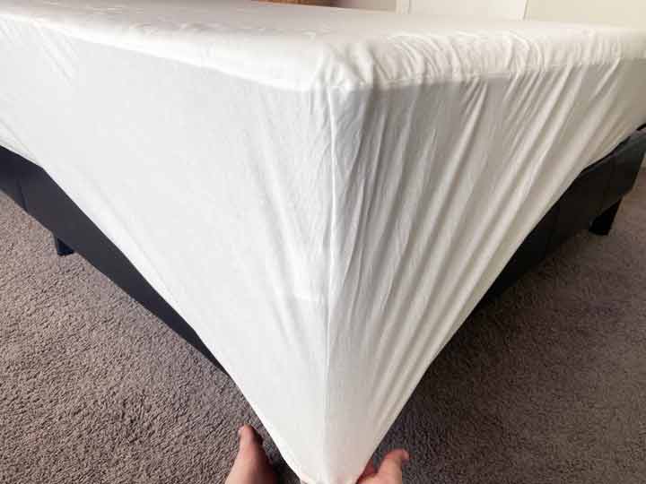 A hand tugs at the corner of the Saatva Mattress protector to show how deep its pockets are.