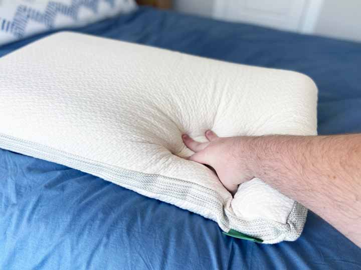 A hand presses into the Avocado Molded Latex Pillow to test its firmness.