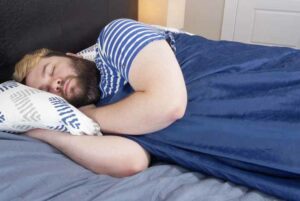 A man sleeps on his side with the Resident Serenity Sleep Weighted Blanket