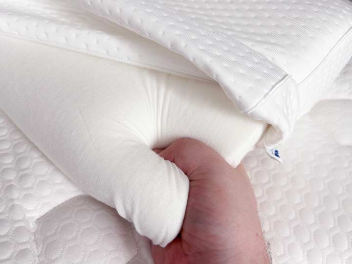 A hand squeezes the memory foam core of the TEMPUR-Neck pillow.