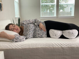 A pregnant woman rests on her side with the Boppy Side Sleeper pillow