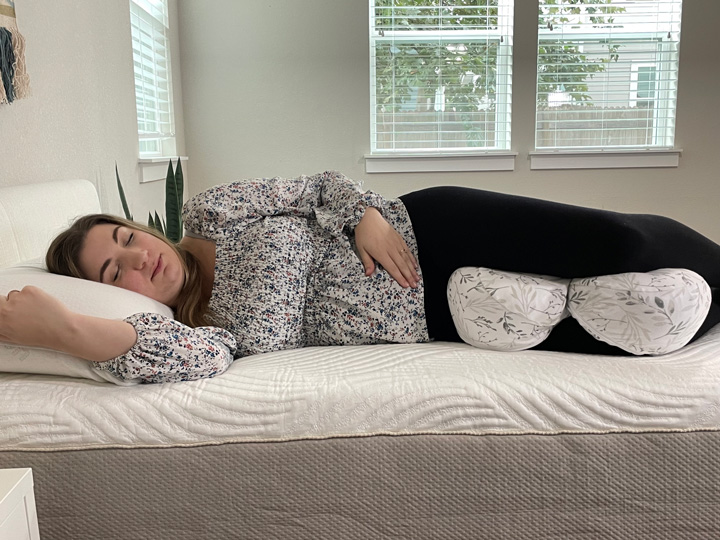 A pregnant woman sleeps on her side with a pregnancy pillow