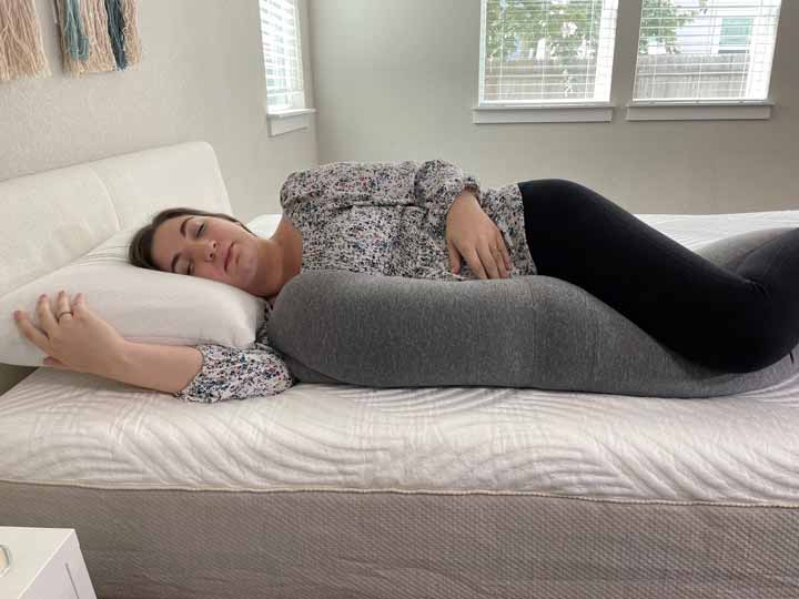 A pregnant woman rests on her side with the Frida Mom pregnancy pillow.