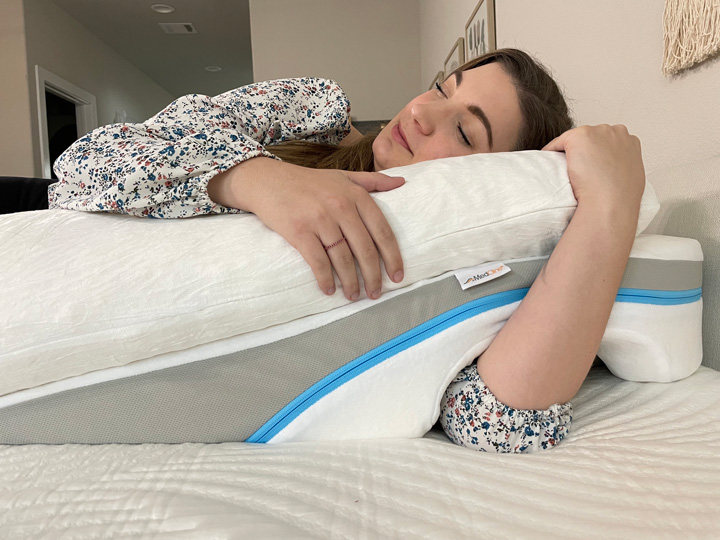 A woman sleeps on her side, threading her arm through the arm gap in the MedCline pillow.