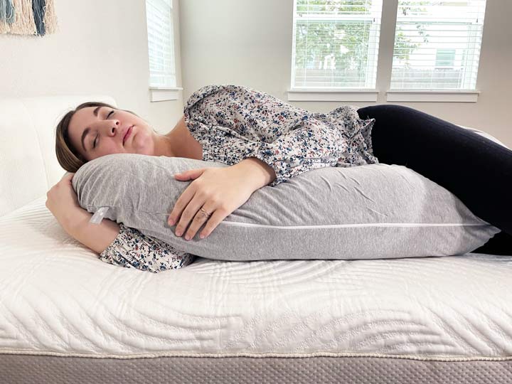 A woman rests on her side while she cuddles the Leachco Snoogle body pillow.
