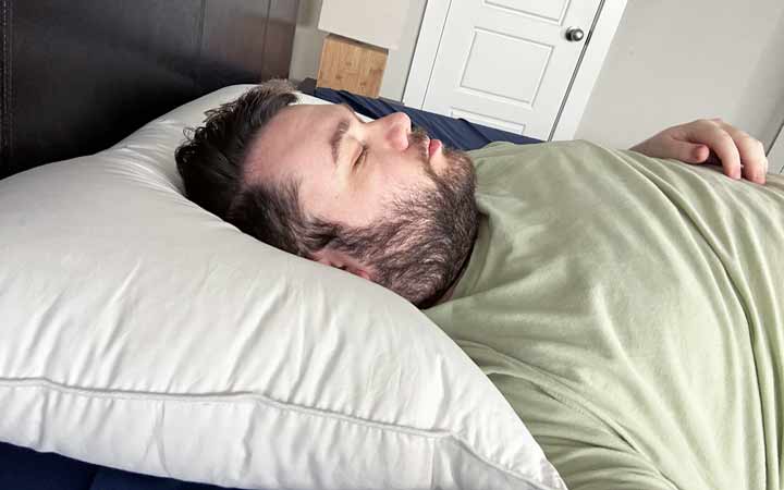 A man sleeps on his back with the Plushbeds White Goose Down Pillow.