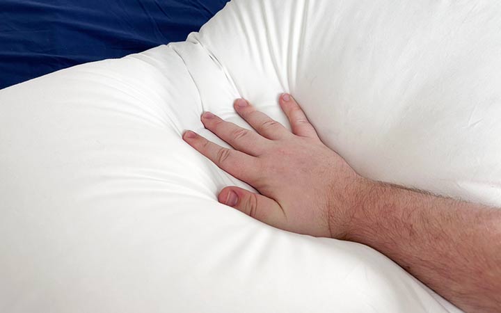 A hand presses into the Plushbeds White Goose Down Pillow.