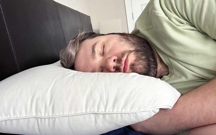 Ein Mann schläft auf der Seite mit dem weißen Gänsedaunenkissen von Plushbeds.