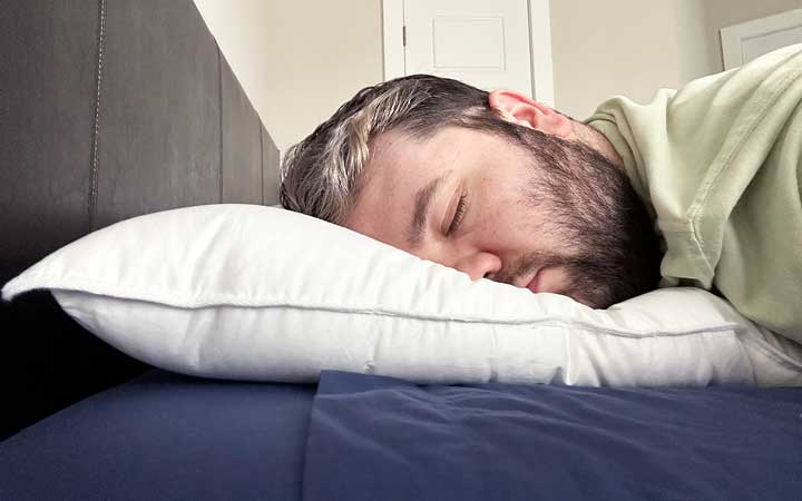 A man sleeps on his stomach while using the Plushbeds Goose Down Pillow.