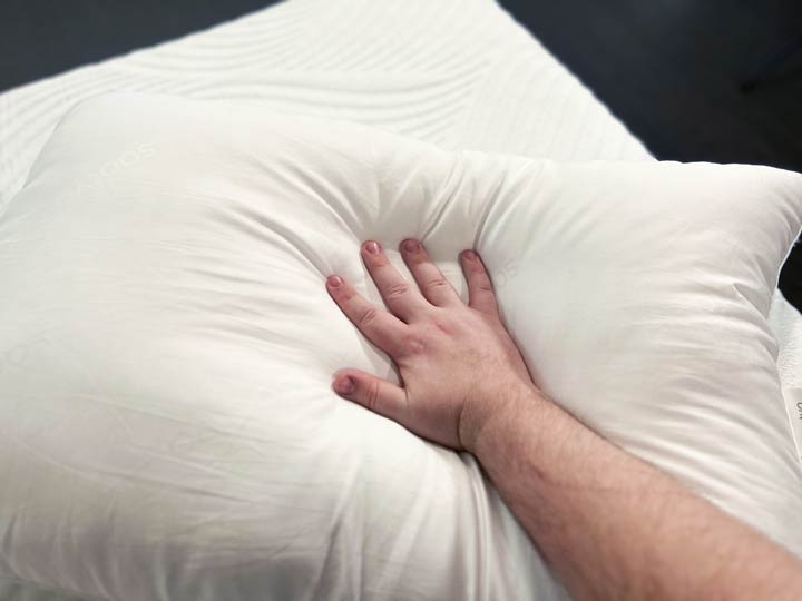 A hand presses into the Saatva Down Alternative Pillow to show off its feel.