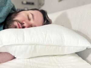 A man sleeps on his side using the Saatva Down Alternative Pillow.