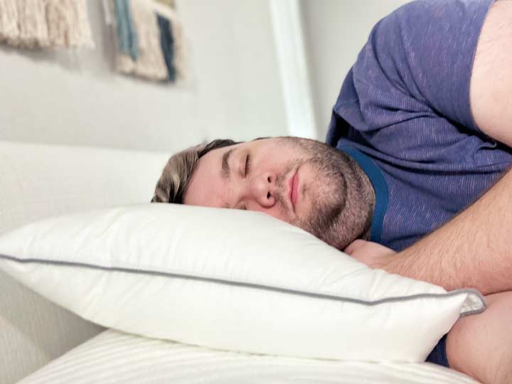 A man sleeps on his side using the Tuft & Needle Down pillow.