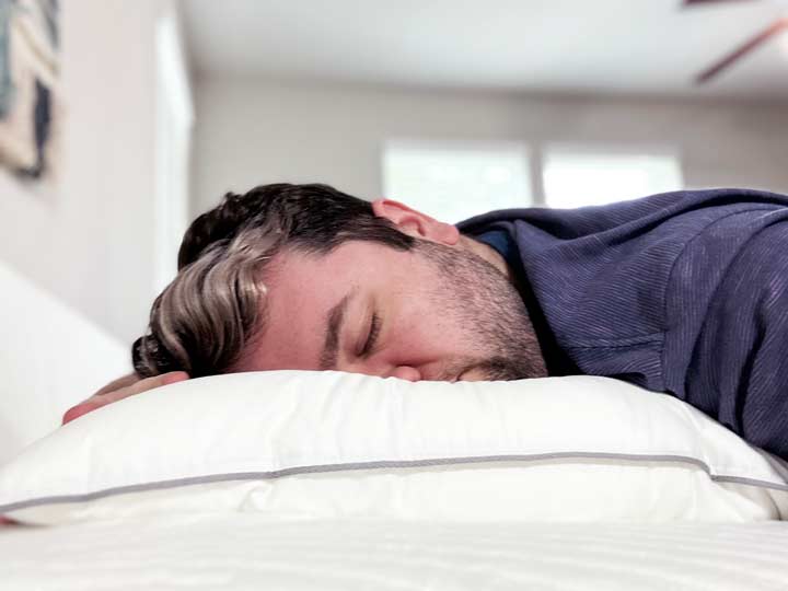 A man rests on his stomach using the Tuft & Needle Down pillow.