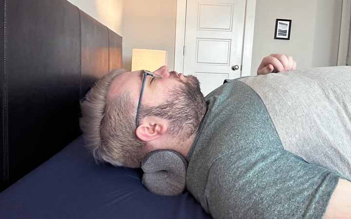 A wide shot of a man resting his head and neck on the NekGenic Neck Pillow.