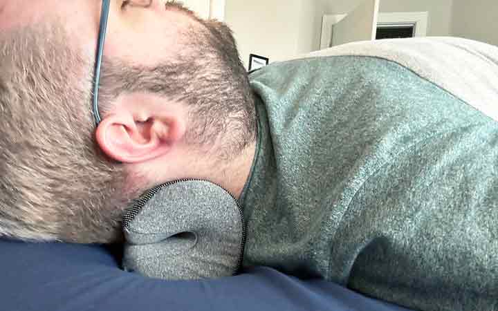 A close up of a man resting his head and neck on the NekGenic Neck Pillow.