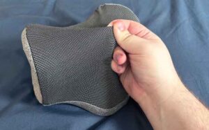 A hand pulls at the gray outer cover of the NekGenic Neck Pillow.