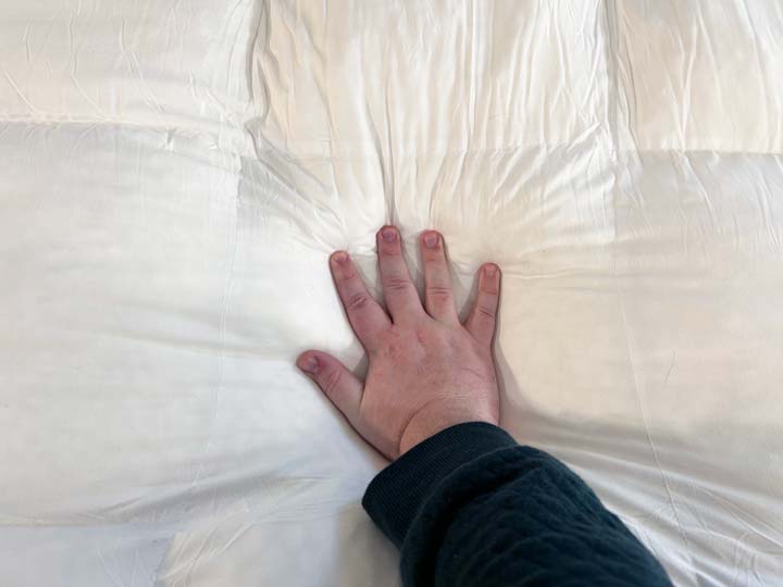 A hand presses into the Coop Home Goods Retreat Mattress Topper.