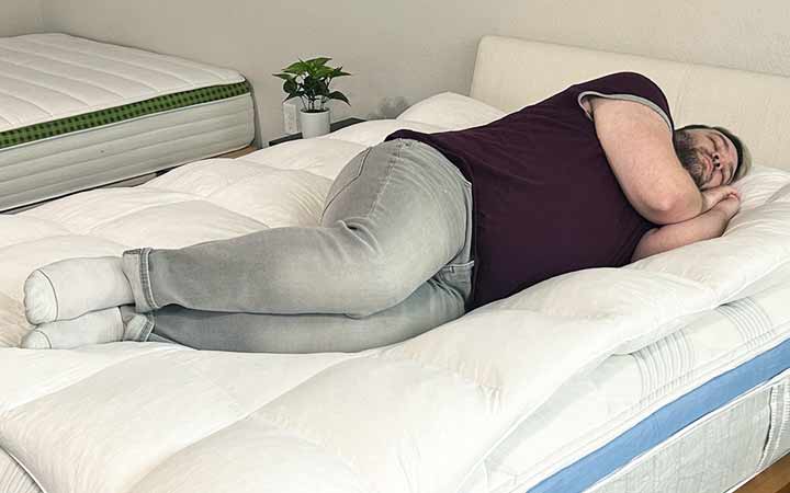 A man sleeps on his side while on top of the Coop Home Goods Retreat Mattress Topper.