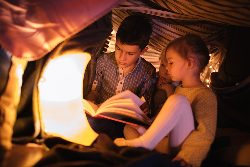 Brother reading a story to his younger siblings in a fort at night